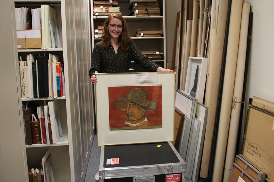 Greenhill holding up framed artwork in UVic Special Collections