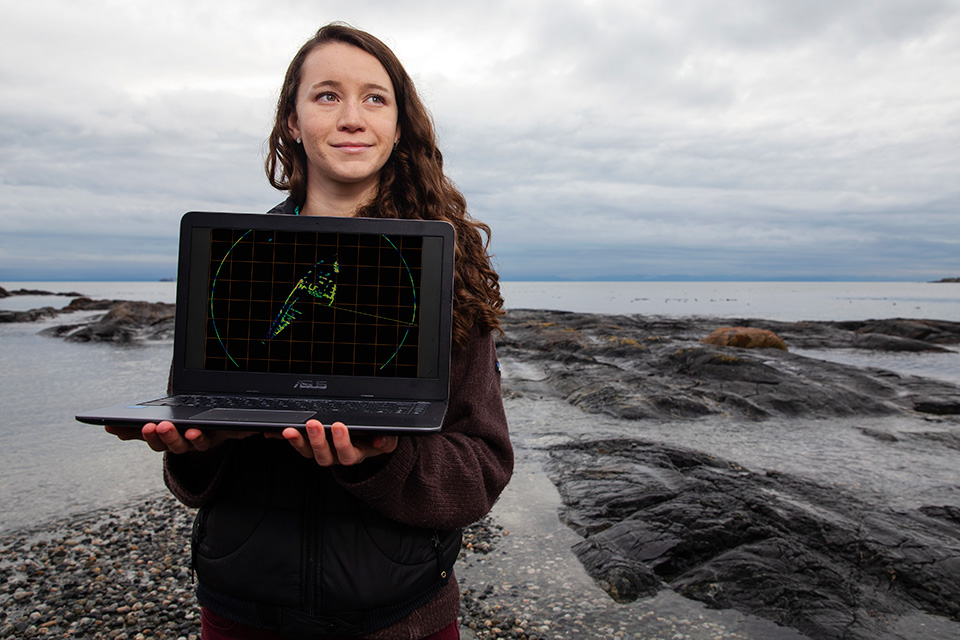 UVic student Desiree Bulger holding a laptop by the ocean