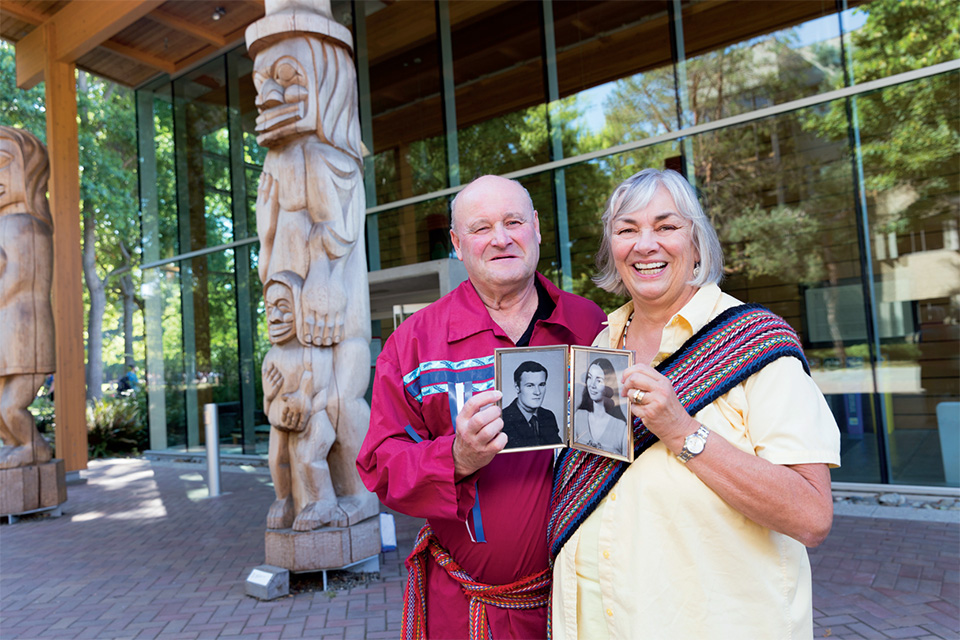 Fern and Mark Perkins outside of UVic's First Peoples House holding old photos of themselves
