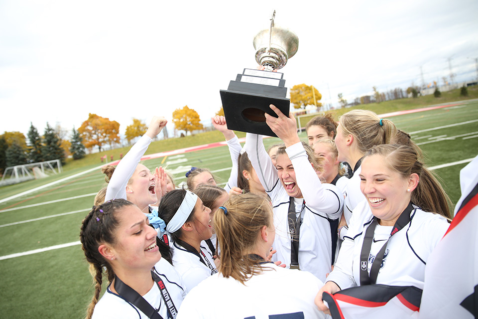 Vikes field hockey team cheering and hoisting the championship banner and cup