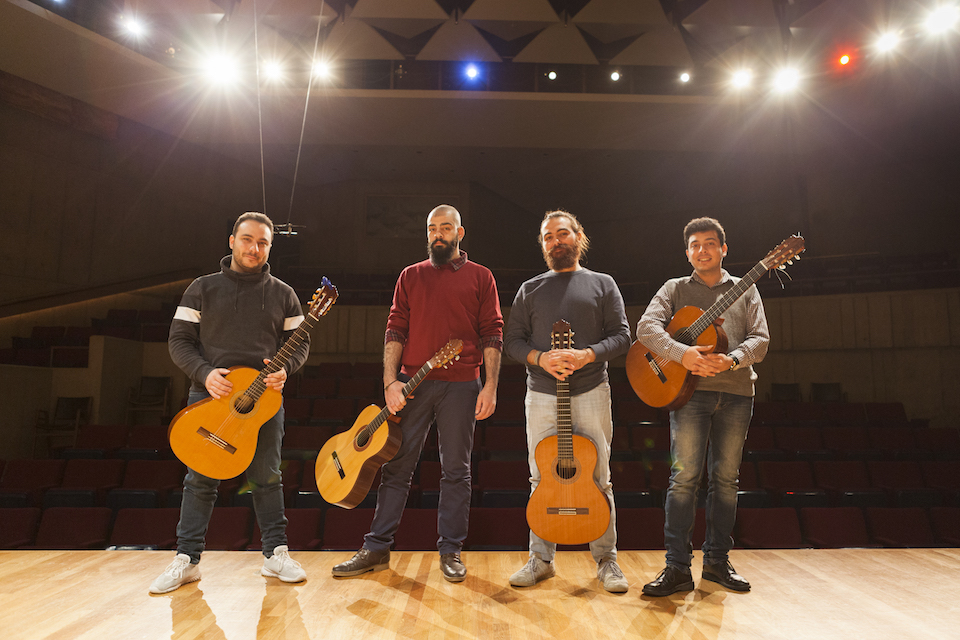 Orontes Guitar Quartet poses on stage with the auditorium seats in the background