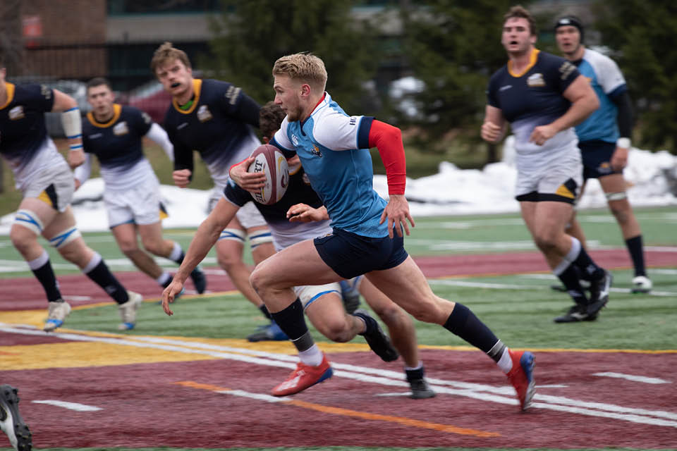 Vikes men's rugby player carries the ball down the field.