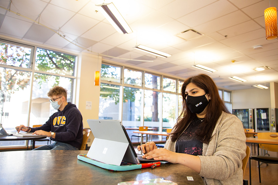 two students sit in study space looking at laptops