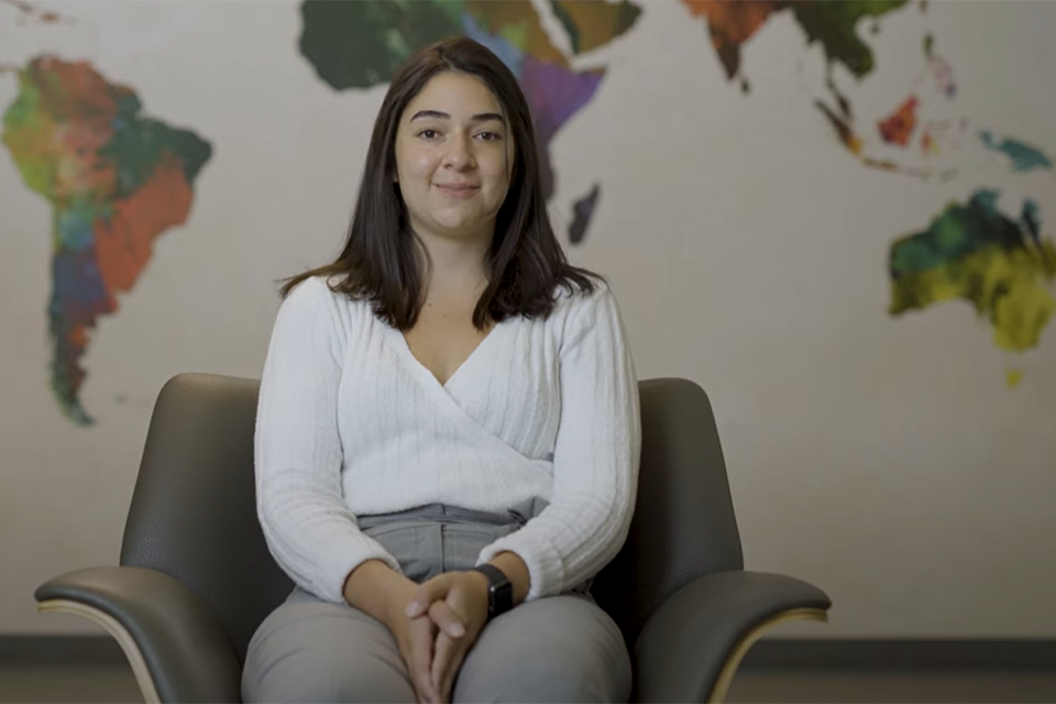Jennifer Ramirez-Betancur, a participant of the Students' Dialogue on Democratic Engagement, gives an interview in front of a colourful world map.