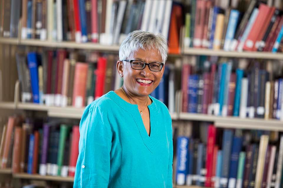 Inba Kehoe poses in front of full bookshelf, smiling brightly.