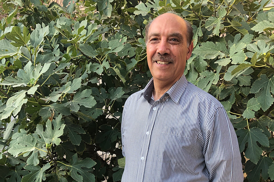 Hossein Nassaji stands in front of green leafy background, smiling.