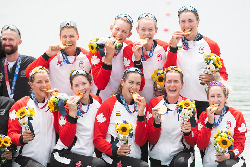 UVic rowing alumna Avalon Wasteneys poses with her team, who just won Gold at the Tokyo 2021 Olympics. They wear the Canadian uniform and playfully bite their Gold medals.
