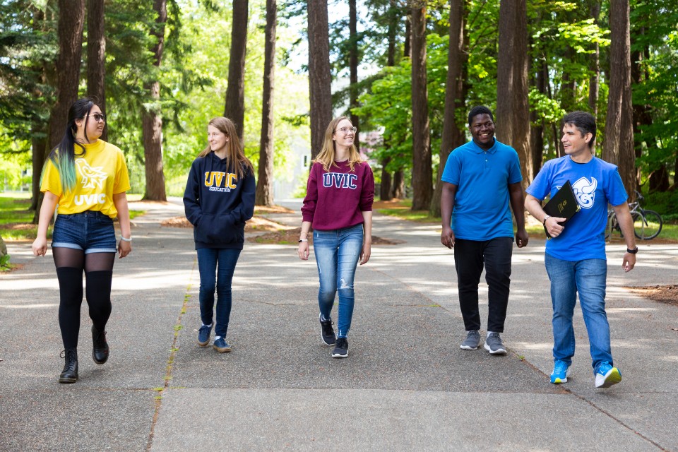 Five students walking along a treed path wearing UVic shirts.