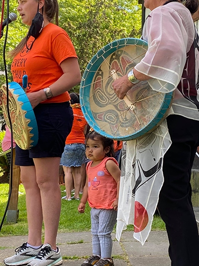 Women standing with drums with a small child looking on