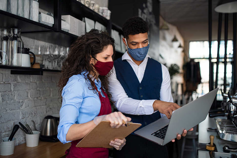 Two baristas with masks looking at laptop in a coffeeshop