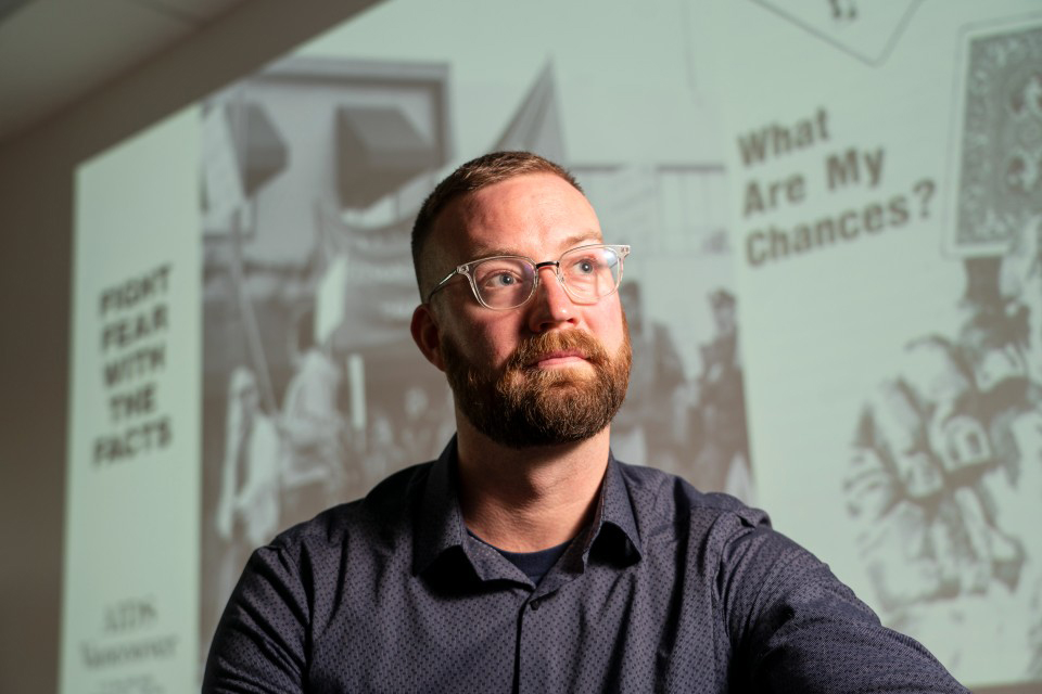 UVic researcher Nathan Lachowsky stands in front of UVic Libraries archival material from the beginning of the HIV/AIDs pandemic.