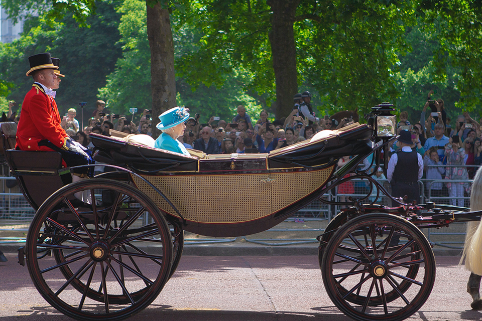 Stock image of the late British queen in a horse-drawn carriage with crowds in the background lining a street.