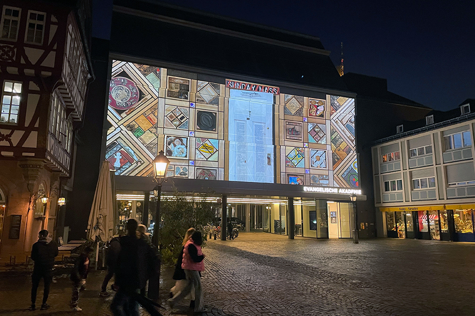The Witness Blanket is displayed in panoramic panels in the glass windows at the Frankfurt book fair at night.