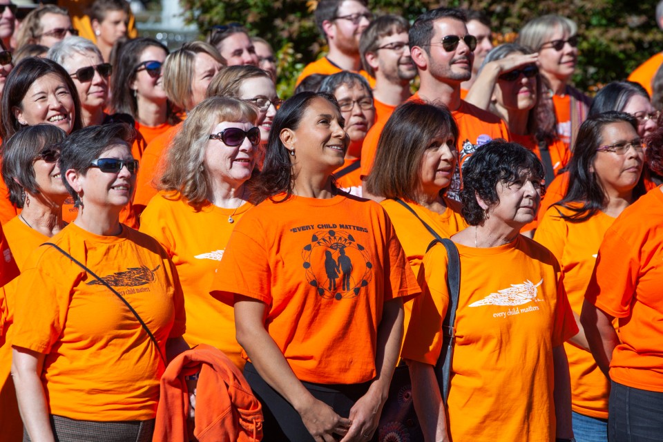 A diverse group of people stand wearing orange shirts and smiling