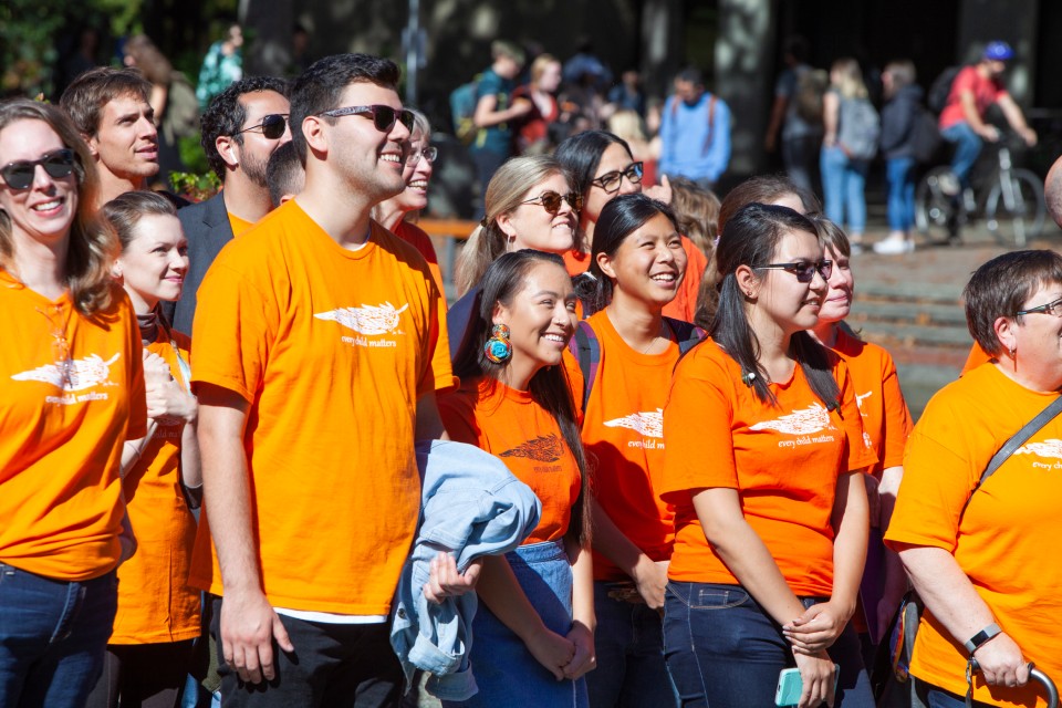 A diverse group of people stand wearing orange shirts and smiling while attending Orange Shirt Day events on UVic Campus