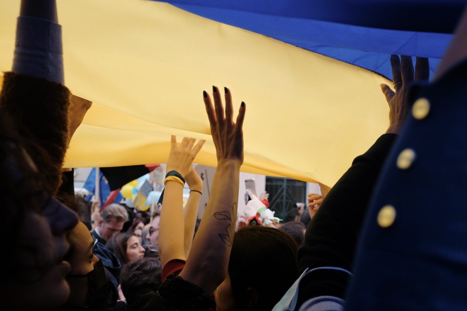 People with hands raised, lifting Ukraine flag in protest against Russian invasion