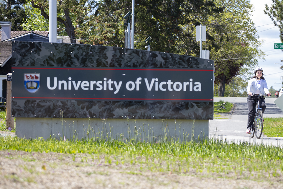 Girl cycles past UVic sign