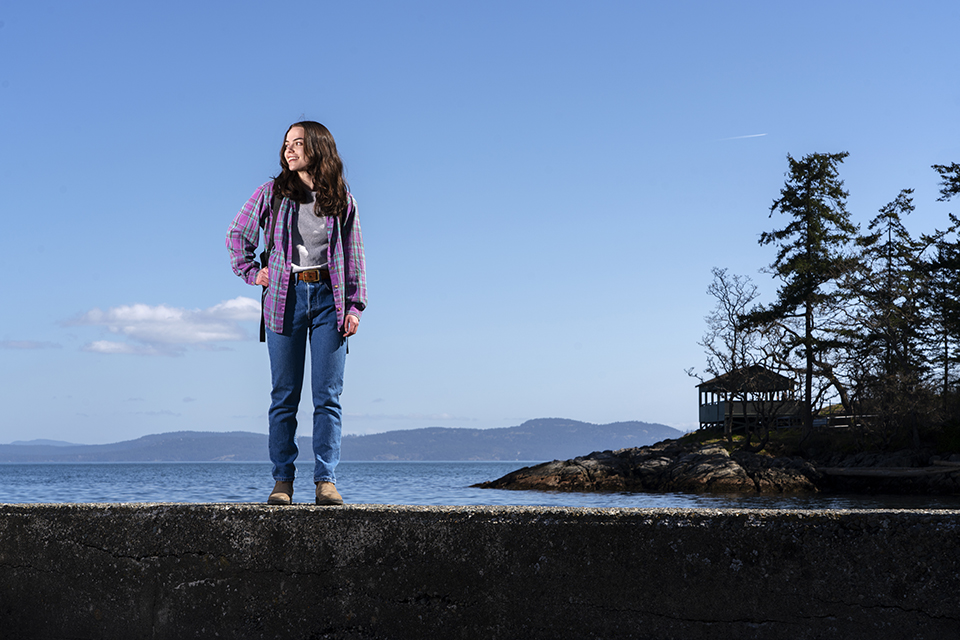 Woman stands on stone breakwater at beach looking to the left of frame