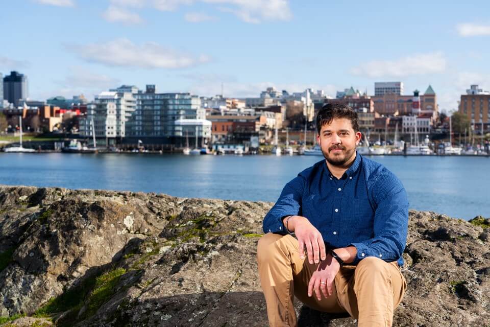 Gerald Singh, UVic assistant professor in the School of Environmental Studies, sits outside on the rocks in the Songhees.