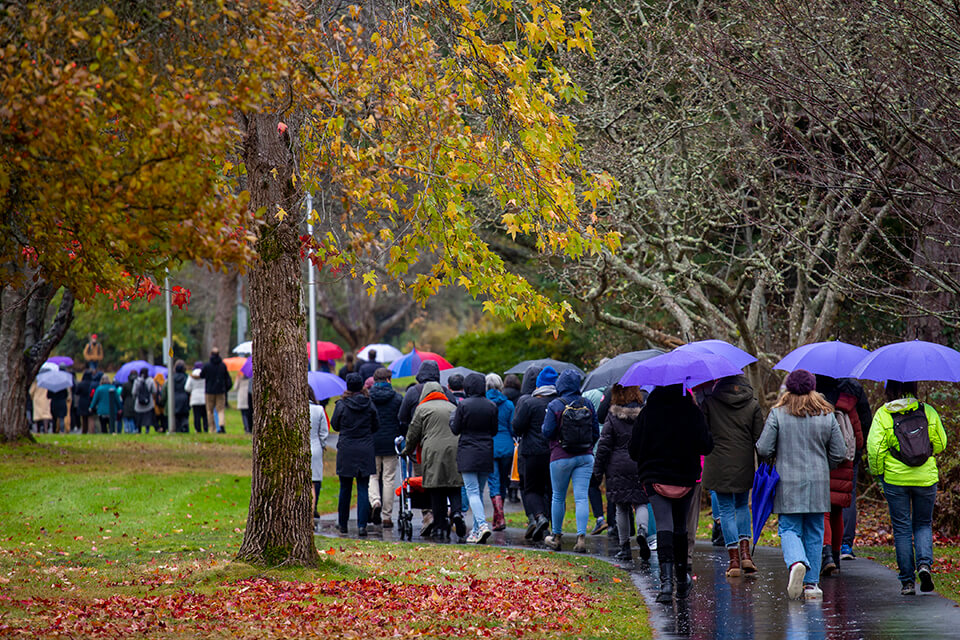 A group of people walk across campus under umbrellas in honour of the National Day of Remembrance and Action on Violence Against Women.