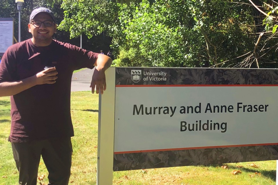 Indigenous law student Dustin Fox stands next to the Fraser Building sign at the University of Victoria