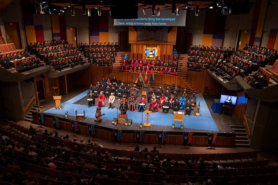long shot of the convocation ceremony stage with designees in full regalia surrounded by graduates in cap and gown