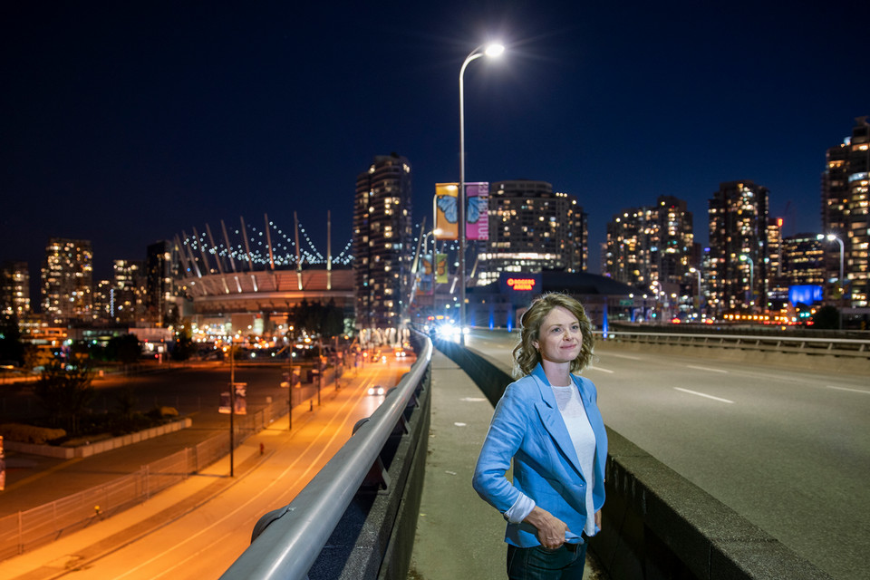 UVic researcher Madeleine McPherson stands on a Vancouver bridge at night with streaks of vehicle tail lights blur past.