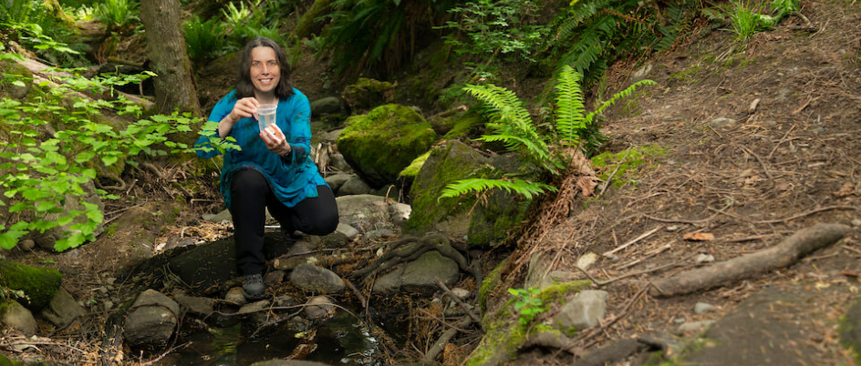 biochemist Caren Helbing kneels in forest with sample
