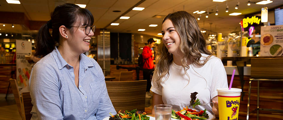 Two UVic students sit in the cafeteria with meals paid for with their ONECards.