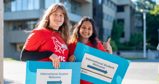 Two international students holding signs saying International Student Welcome and smiling