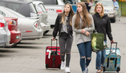 Three women rolling suitcases towards residence