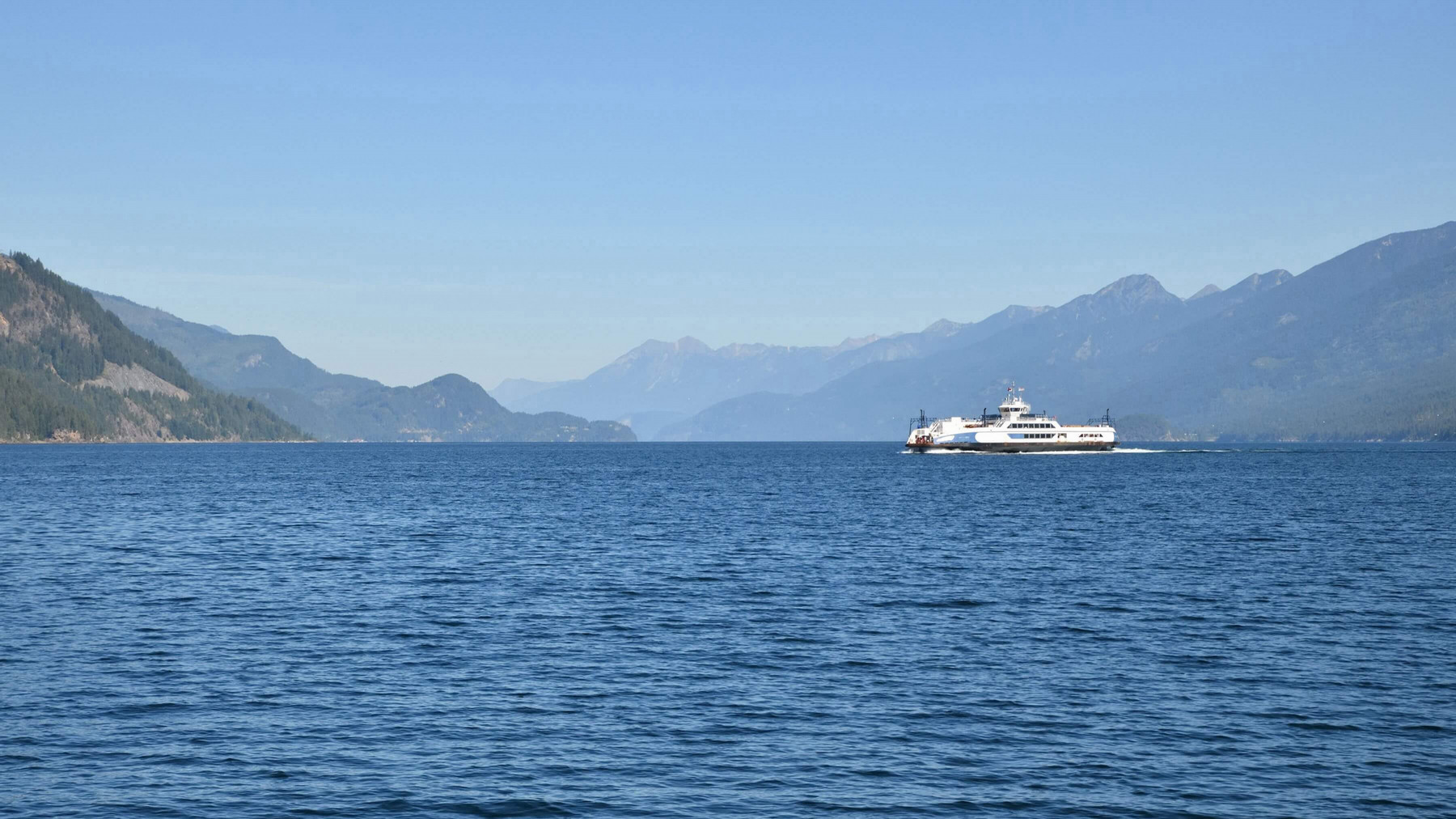 Photo of a ferry on a lake, with mountains in the background