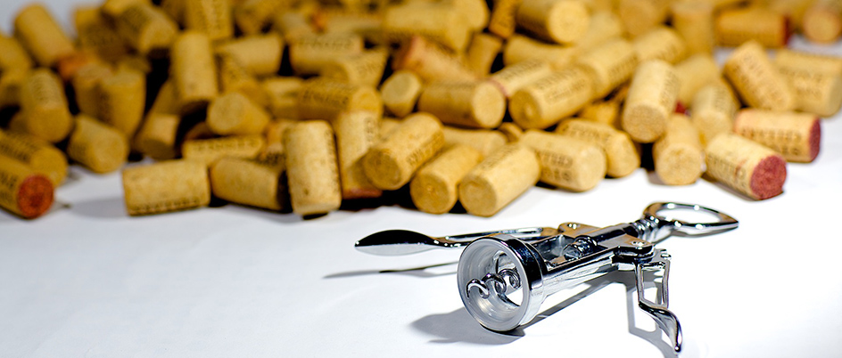 An image of a corkscrew in front of a pile of wine corks