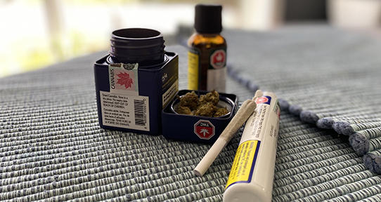 A photo of dried cannabis, a cannabis joint and packaging on a table.