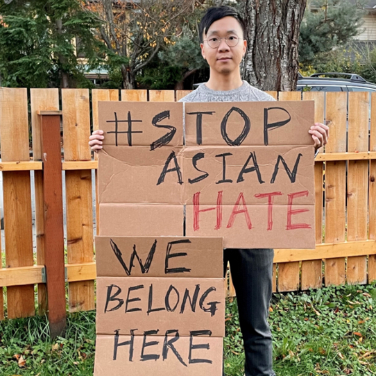Nigel holding a sign that says "#Stop Asian hate - we belong here"