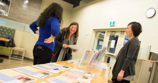 CFYS research assistants Hannah Kim and Emerald Pringle discuss research briefs with a community member at a CFYS event.