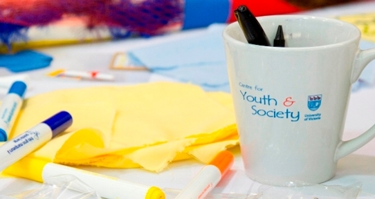 Closeup of a CFYS mug on a desk covered in papers and pens.