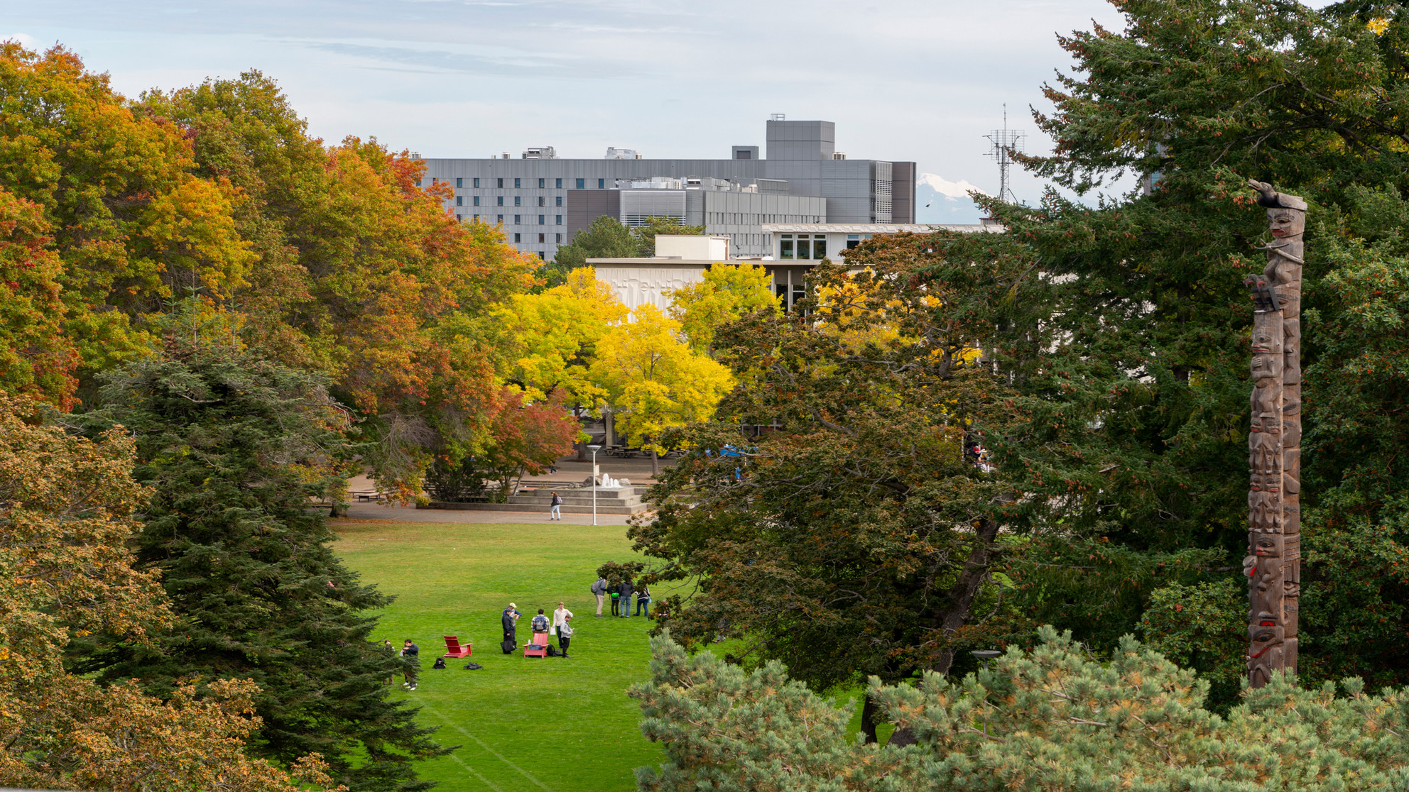 UVic campus viewed from afar, with people gathering on a grassy field surrounded by trees with autumn foliage.