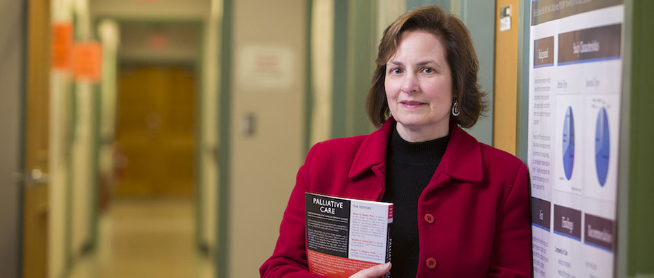 A photo of Kelli Stajduhar standing in a hallway in a red blazer holding a book