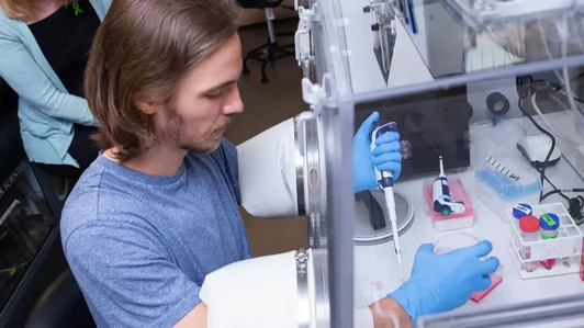 Side view of a male student pipetting inside a glove box