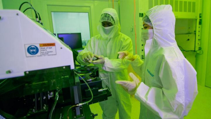 Two researchers in biohazard suits work in a CAMTEC lab space