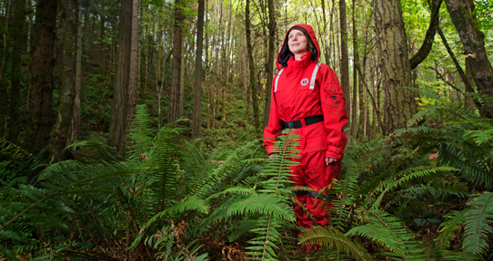 Graduate Earth and ocean sciences student Kristen Kanes in the forest wearing a red ocean suit