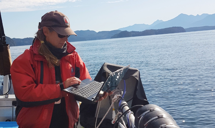 Rhonda Reidy on a boat using a laptop, researching humpback whales