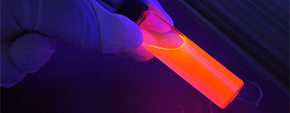 Gloved hand holding a vial with an orange liquid