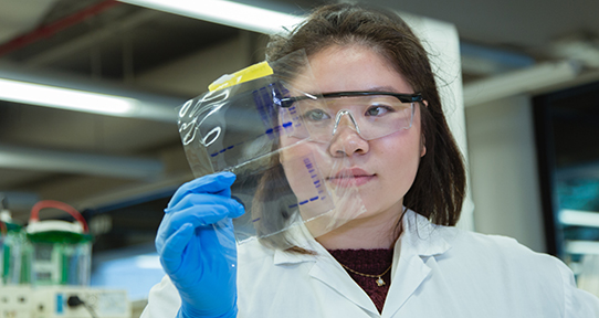 Student holding up and looking at a sample protected with plastic in a lab