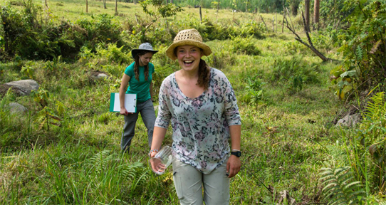 Navarana Smith holding a beaker and walking through a field in Uganda