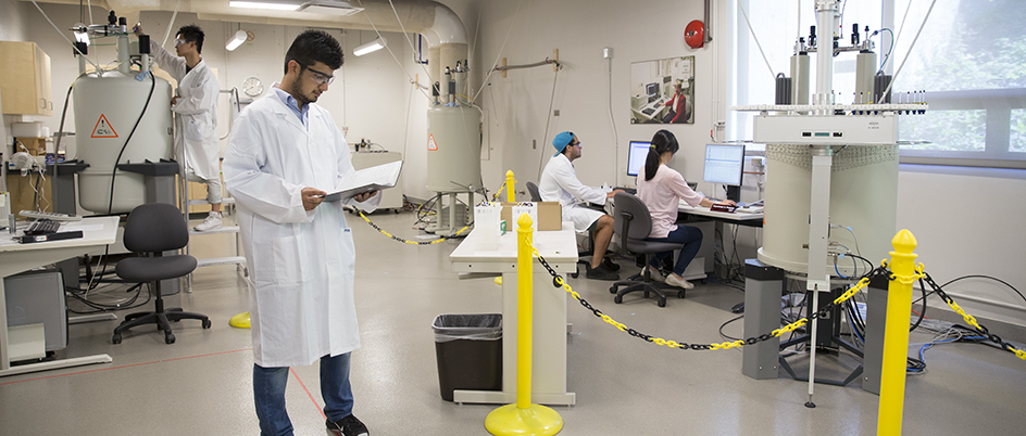 Man in a lab dressed in a white lab coat looking at a notebook