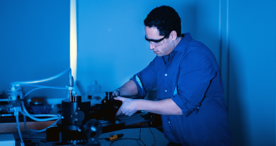 Graduate student in a lab working with equipment in a blue-lit room