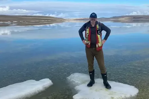Zurek in rubber boots and a safety vest standing on ice in water. 
