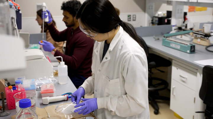 A female student in white lab coat preparing petri dishes at a bench